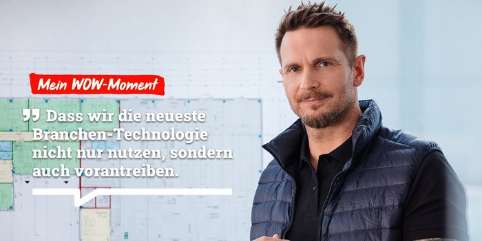 Der Mann trägt eine Weste und spricht über die Nutzung neuer Branchentechnologien, die auf dem Plan hinter ihm sichtbar sind.